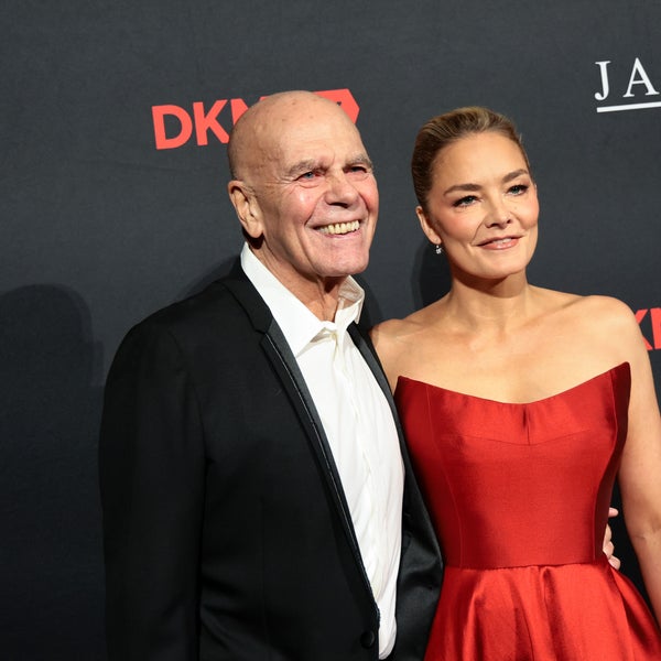 Peter Harf and Katharina Harf pose together on a red carpet in front of a black backdrop with DKMS and JAB logos. Peter Harf wears a black tuxedo, and Katharina Harf wears a strapless red gown. Both are smiling. Peter Harf and Katharina Harf pose together on a red carpet in front of a black backdrop with DKMS and JAB logos. Peter Harf wears a black tuxedo, and Katharina Harf wears a strapless red gown. Both are smiling.