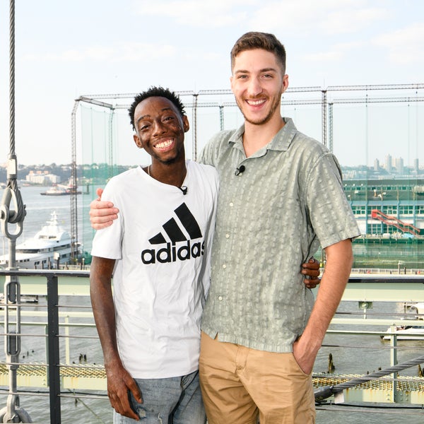 Two smiling young men, who are donor and patient, stand side by side on a platform with their arms around each other. The guy on the left wears a white Adidas t-shirt, the other one on the right a light green patterned shirt and beige shorts. In the background, a river, boats, and a city skyline are visible. Two smiling young men, who are donor and patient, stand side by side on a platform with their arms around each other. The guy on the left wears a white Adidas t-shirt, the other one on the right a light green patterned shirt and beige shorts. In the background, a river, boats, and a city skyline are visible.