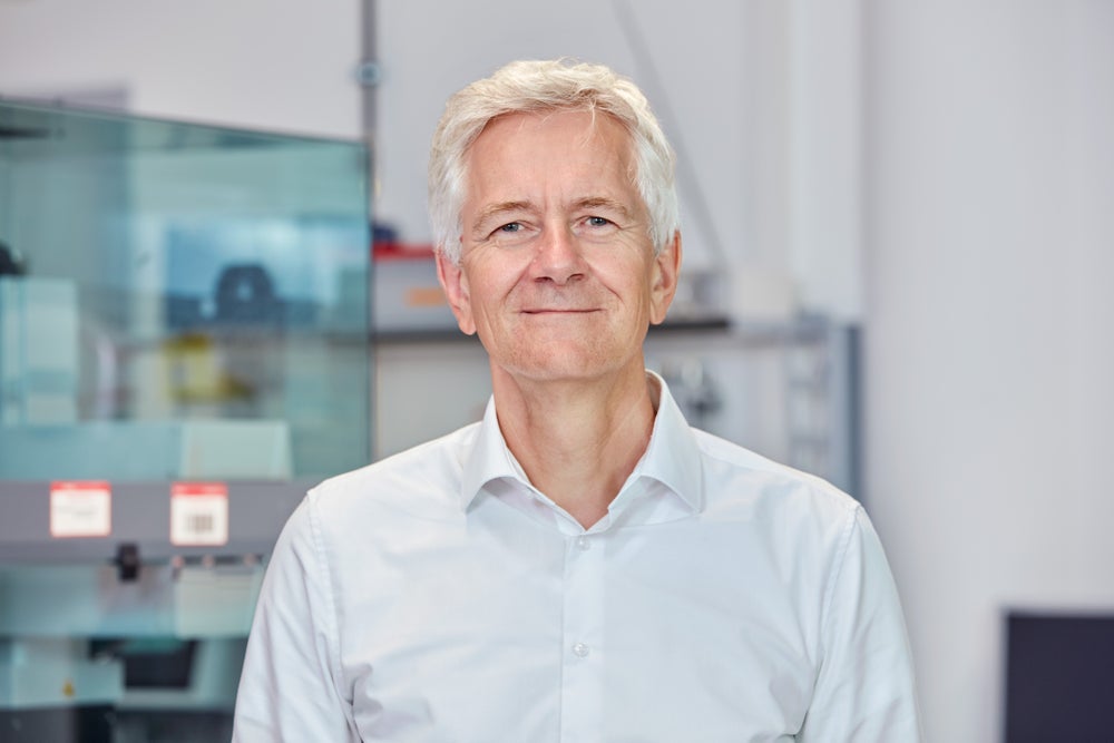 Prof. Dr. Johannes Schetelig, Global Chief Scientific Officer of DKMS, smiles gently at the camera while standing in a bright laboratory setting. Prof. Dr. Johannes Schetelig, Global Chief Scientific Officer of DKMS, smiles gently at the camera while standing in a bright laboratory setting.