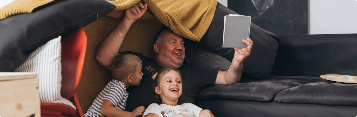 Man reading a book to 2 children while smiling and laughing.