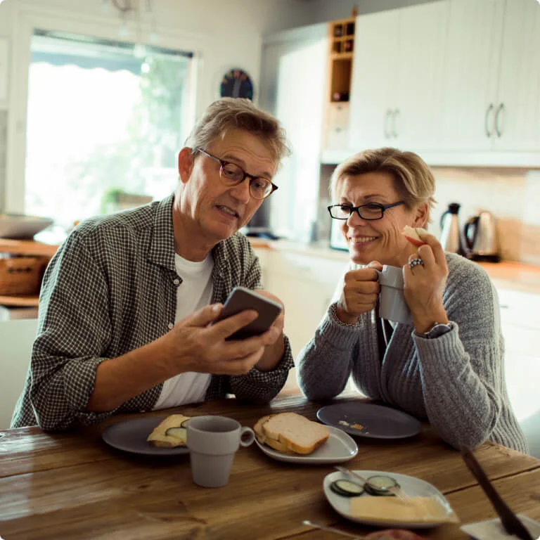 Couple enjoying food and drinking tea at a table while smiling at a phone.