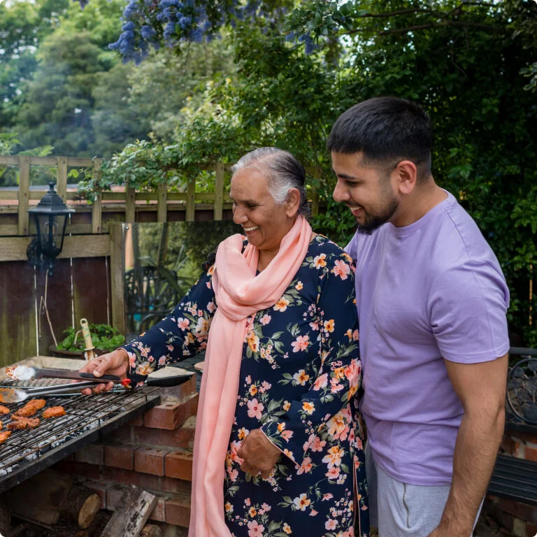 Mother and son cooking a barbeque in the garden while smiling.