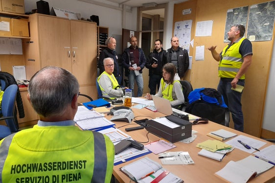Mitarbeiter der Alperia (stehend in der Mitte) nahmen als Beobachter an der Hochwasserübung teil; stehend ganz rechts der Organisator der Hochwasserübung und für die Lageführung Verantwortliche Hansjörg Prugg, ganz links der Direktor des Funktionsbereichs Wildbachverbauung Fabio De Polo (Foto: LPA/Maja Clara)