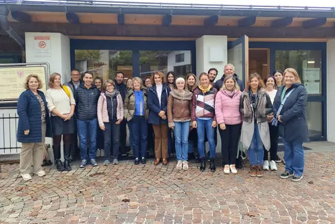 Gruppenbild der ladinischen Delegation vor der Grundschule in Sankt Felix am Deutschnonsberg (von links nach rechts): Edith Ploner, Dagmar Morandell, Heinrich Videsott, Elvis Burchia, Adele Piazzi, Agnes Irsara, Bernhard Flatscher, Genny Ploner, Monica Moroder, Flavia Lardschneider, Maria Kostner, Susy Rottonara, Sofia Stuflesser, Irene Kostner, Veronica Rubatscher, Lorenz Clara, Albert Videsott, Petra Senoner, Romy Canins, Edith Kofler, Federica Piffer und Maria Teresa Mussner (Foto: LPA/Direktion Ladinische Bildung und Kultur)