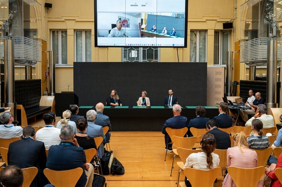 Adrian Plessin, Leiter der Abteilung für Wirtschaftsförderung des Landes Kärnten (Österreich, rechts am Tisch), Andreas Meyer, technischer Leiter von WSW mobil GmbH (Deutschland, per Videokonferenz zugeschaltet) und die Präsidentin der SASA AG Astrid Kofler (links am Tisch), tauschten sich im Rahmen einer Podiumsdiskussion aus, die von Elisabeth Stampfer von der SASA AG moderiert wurde. (Foto: LPA/Fabio Brucculeri)