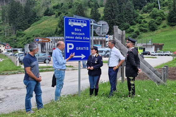 Der Direktor des Straßendiensts Götz Rufinatscha, Bürgermeister Giorgio Costabiei, die Leiterin der Straßenpolizei in Südtirol Katia Grenga, Landesrat Daniel Alfreider und Carabinierimajor Innocenzo Colonna besprechen die neue Beschilderung in Pikolein, die Besucher informieren soll, dass das Auto kostenfrei geparkt und der Bus genutzt werden kann, um aufs Würzjoch zu gelangen. (Foto: LPA/Angelika Schrott)
