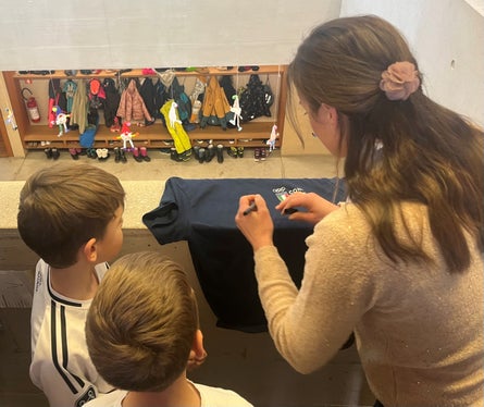 Karin Oberkofler firma una maglietta destinata ad uno degli alunni della scuola primaria di Santa Maddalena, uno dei 70 istituti altoatesini coinvolti nel 2025 da questa iniziativa dedicata al valore dello sport e dei Giochi Olimpici. (Foto: USP)