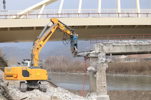 Heute hat das Bauunternehmen Misconel aus Cavalese (mit einer Niederlassung in Bozen) mit dem Abtragen der alten Brücke über die Etsch in Neumarkt begonnen; im Hintergrund die höher gelegene neue Brücke ohne Pfeiler im Flussbett. (Foto: LPA/Maja Clara)