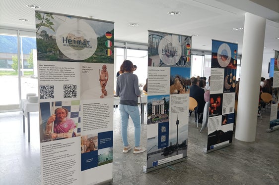 Einblick in die Wanderausstellung Heimat – regionale Identität in Europa mit Publikum im Hintergrund bei der Ausstellungseröffnung am 5. Mai im Oberschulzentrum Mals (Foto: LPA/Fachschule Tisens)