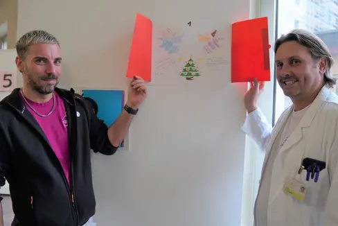 Alex Staffler e Davide Gianotti, Primario e Coordinatore tecnico-assistenziale del Reparto di neonatologia e terapia intensiva neonatale alle prese con il calendario d'Avvento donato dai bambini della scuola primaria Galilei di Merano. (Foto: ASP/Direzione istruzione e formazione italiana)