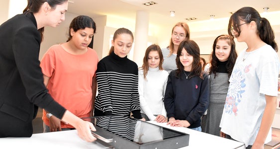 Zeitreisen durch Themen und Projekte der Euregio: Mitarbeiterin Sarah Müller (l.) erklärt Schülerinnen den digitalen „Schlitten“ der Euregio-Ausstellung in Innsbruck. (Foto: Land Tirol/Sidon)
