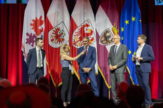 Da sinistra l'assessore trentino Simone Marchiori, il presidente della Provincia autonoma di Bolzano Arno Kompatscher e il presidente del Tirolo Anton Mattle con la presentatrice Karin Gschnitzer. (Foto: Land Tirol/Die Fotografen)