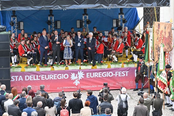 Die Euregio-Landeshauptleute (v. l.) Mattle, Kompatscher und Fugatti auf der Festbühne vor dem Sinfonischen Blasorchester der Tiroler Musikkapelle Wilten (Foto: Landespresseamt Trentino Corrado Poli)