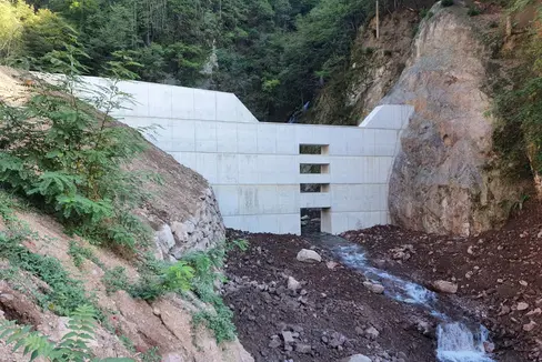 La nuova barriera di contenimento lungo il rio Sinigo è stata ultimata: la struttura è alta 12 metri nella sezione di uscita e 15 metri nell'ala laterale, è larga circa 40 metri e ha uno spessore in cemento armato di due metri e mezzo alla base (Ufficio sistemazione bacini montani Sud)