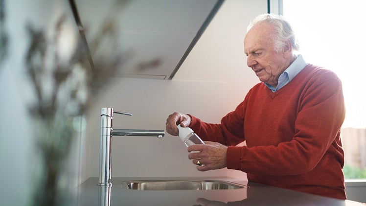 Oudere man vult waterfles in keuken