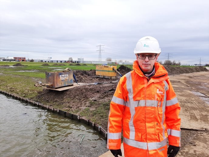 Man in Evides werkkleding poserend voor een bouwplaats