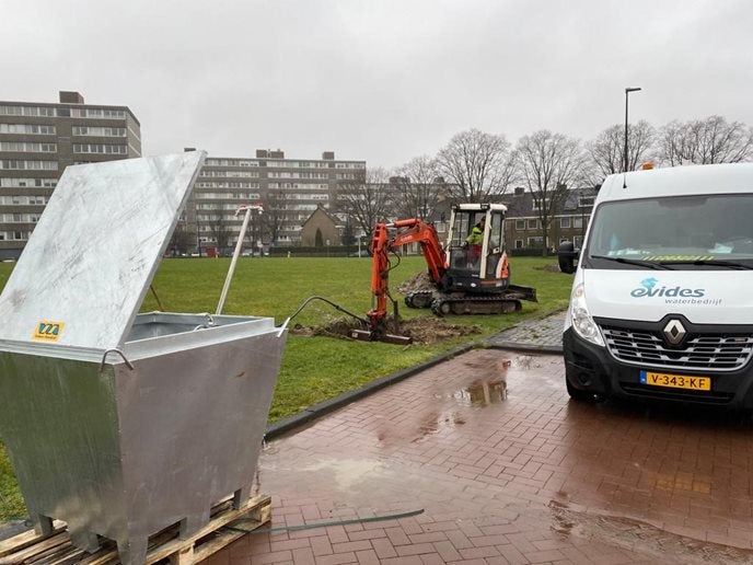 Evides Waterbedrijf werkbus, een graafmachine en een container. Aanleggen van een nieuwe drinkwateraansluiting.