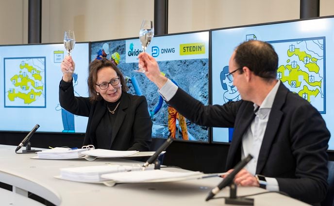 2 mensen heffen een glas champagne in de lucht met getekende contracten op tafel