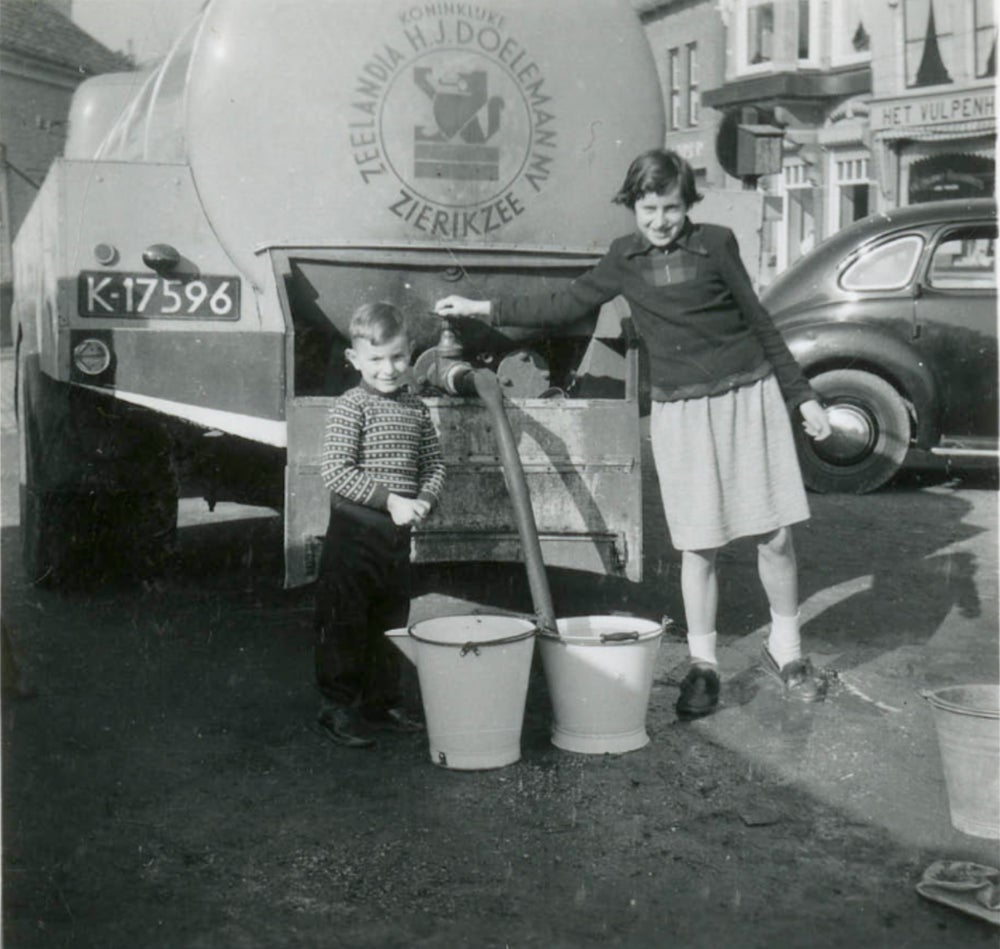 Twee kinderen staan naast een tankwagen met nooddrinkwater.