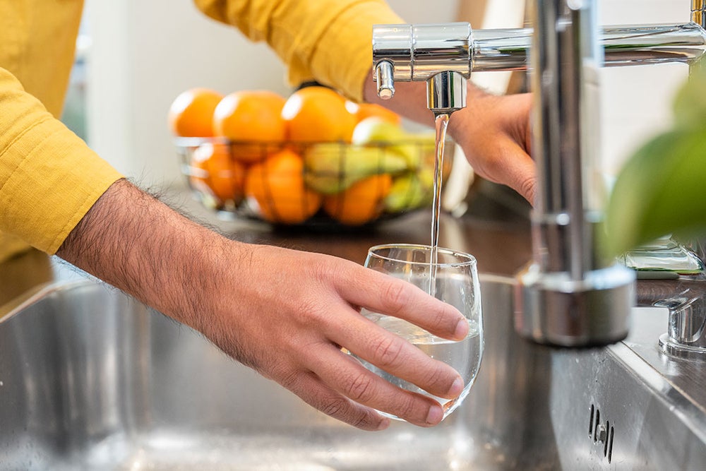 Een hand die een glas water vult onder de kraan