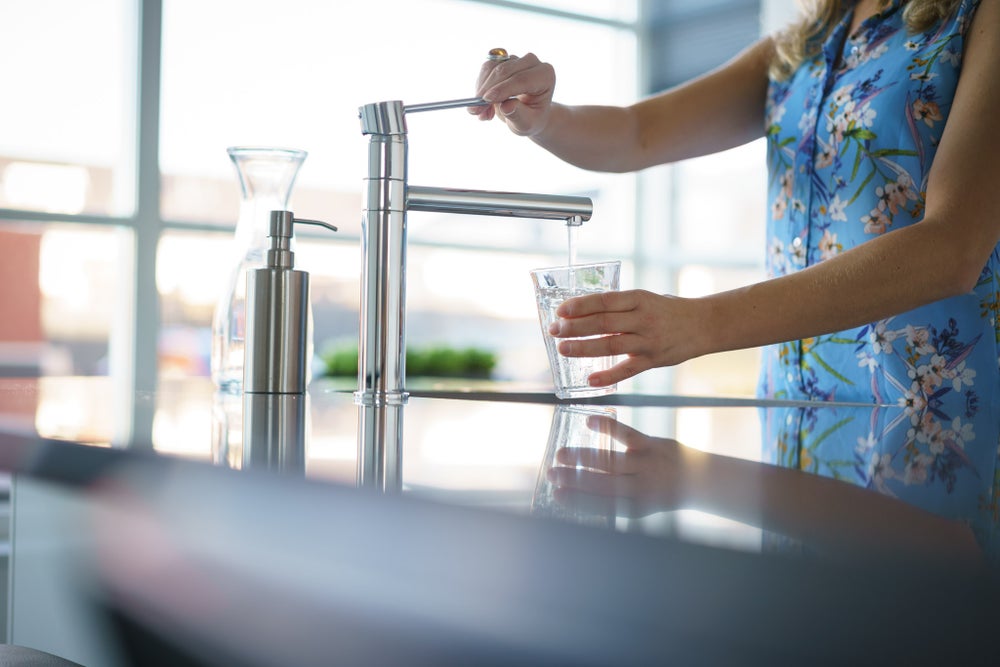 Vrouw vult glas water onder de kraan.