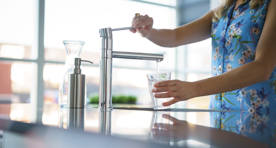 Vrouw vult glas met water onder de kraan