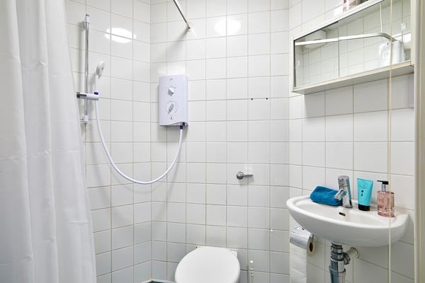 A white bathroom with shower, sink unit, WC and mirrored cupboard on the wall.