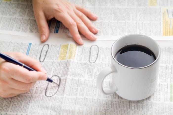 A close up of someone circling job ads in the paper with a cup of coffee