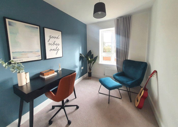 A study room with two chairs, a desk and guitar propped up against a wall.