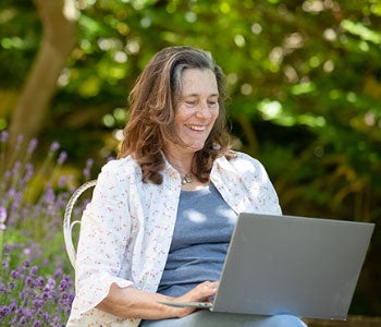 A woman sitting in a garden looking at a laptop