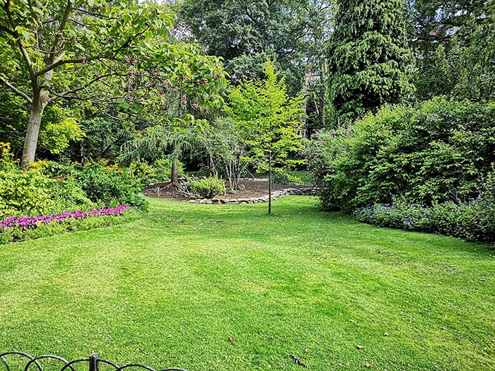 Well maintained landscaped garden with neatly manicured grass in the foreground and a variety of plants, trees and shrubs in the background