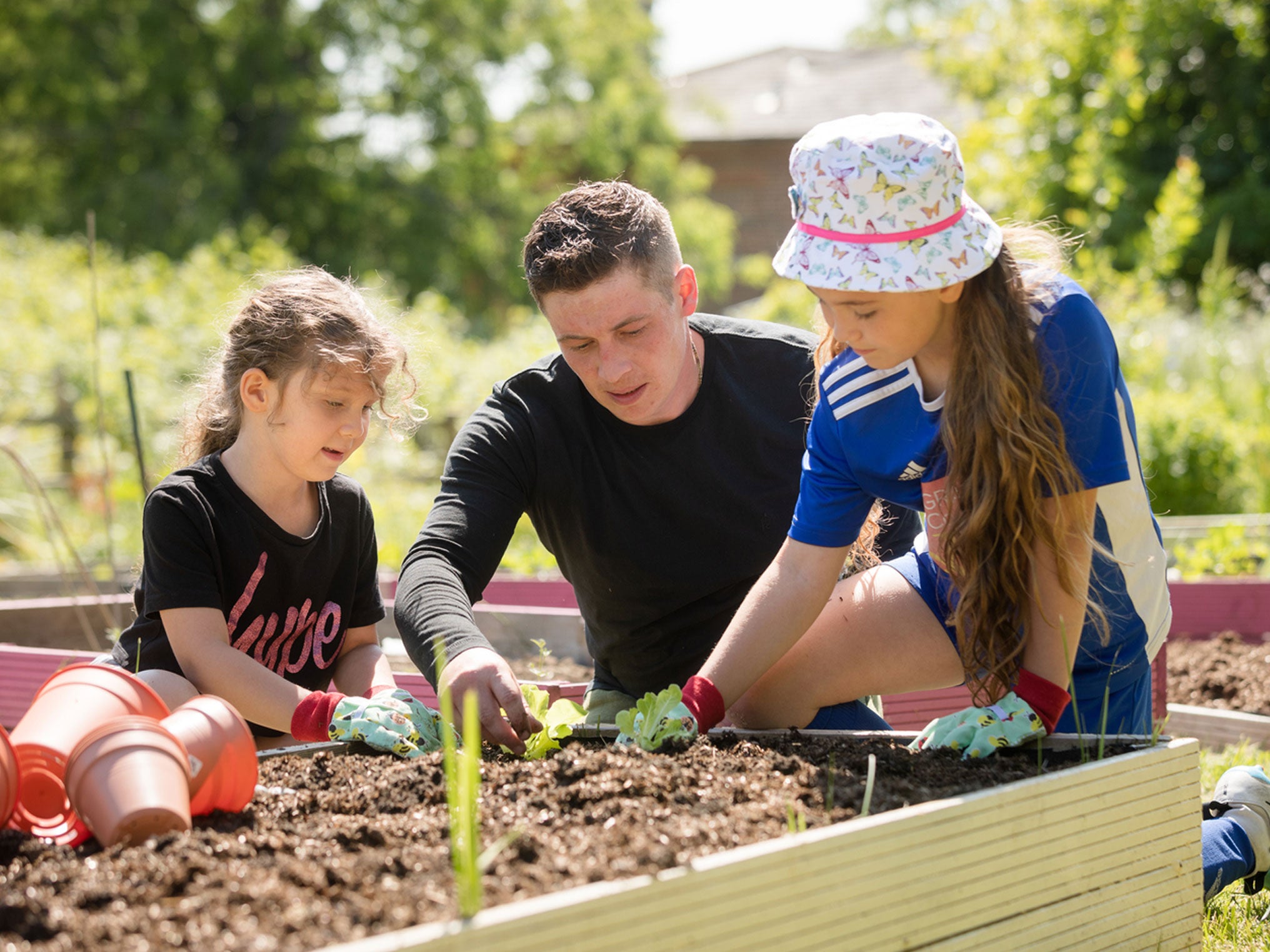 Father and daughters planting vegetables in a planter
