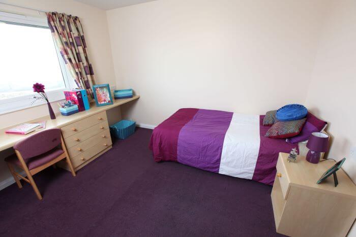 A bedroom with a bed, desk and chest of drawers