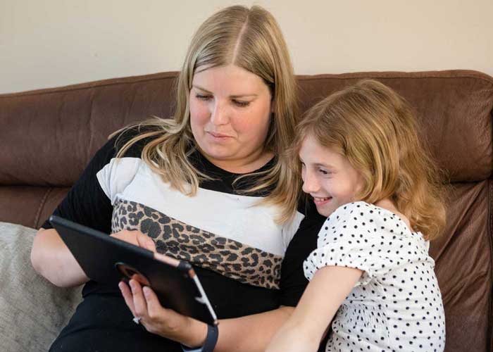 Mother and daughter sitting on a sofa looking at a tablet device.