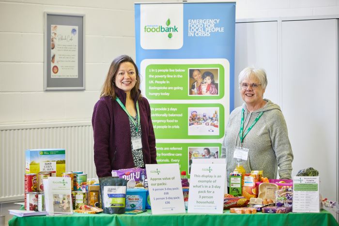 Two ladies standing behind a table at an event with an exhibition board behind them