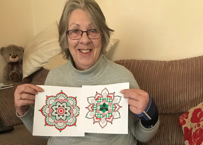 Elderly lady sitting on a sofa and holding pictures towards the camera