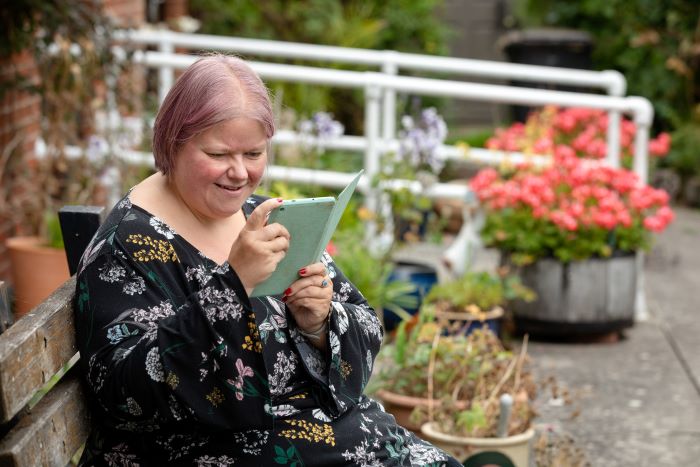 A lady sitting in a garden looking at a Kindle