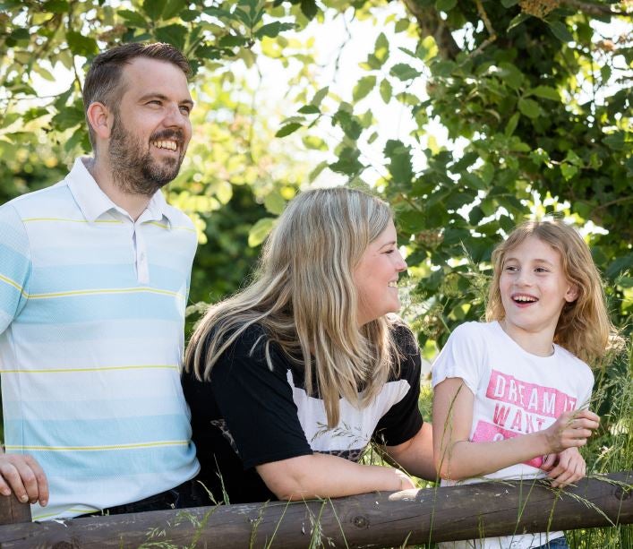 Father, mother and daughter leaning against a fence 