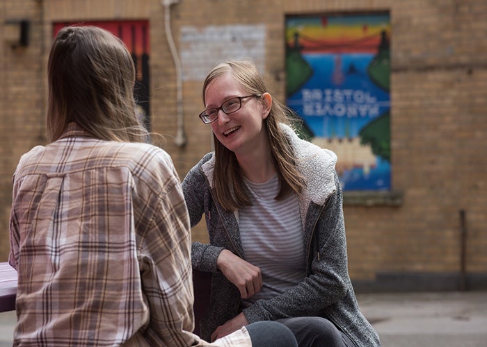 Two girls sitting on a bench, talking.