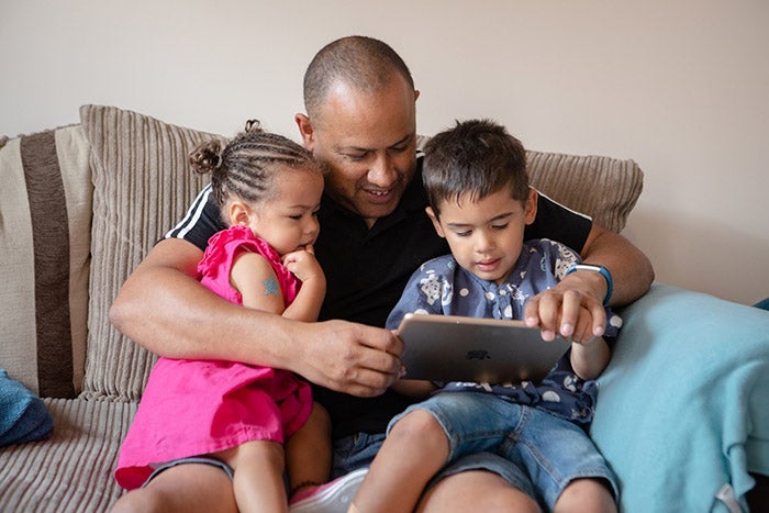 Father, son and daughter sitting on a sofa, looking at an iPad.