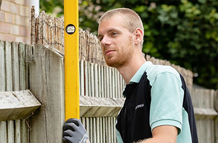Trades employee holding a large yellow spirit level against a fence