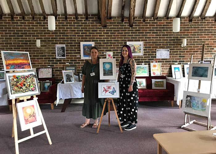 Two women standing by some paintings at an art exhibition