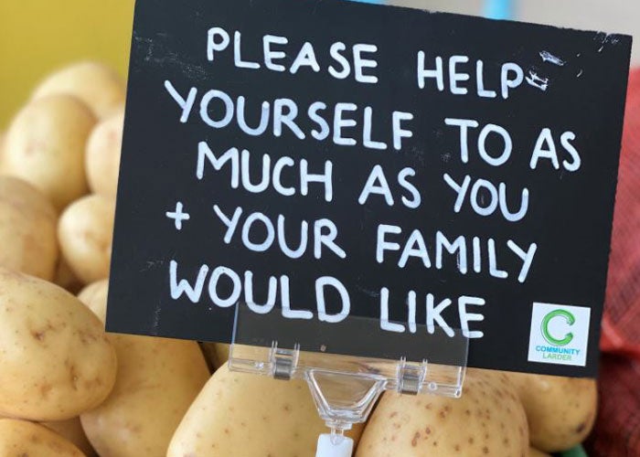 Close up image of a box of potatoes with a sign in them saying 'Please help yourself to as much as you and your family would like'