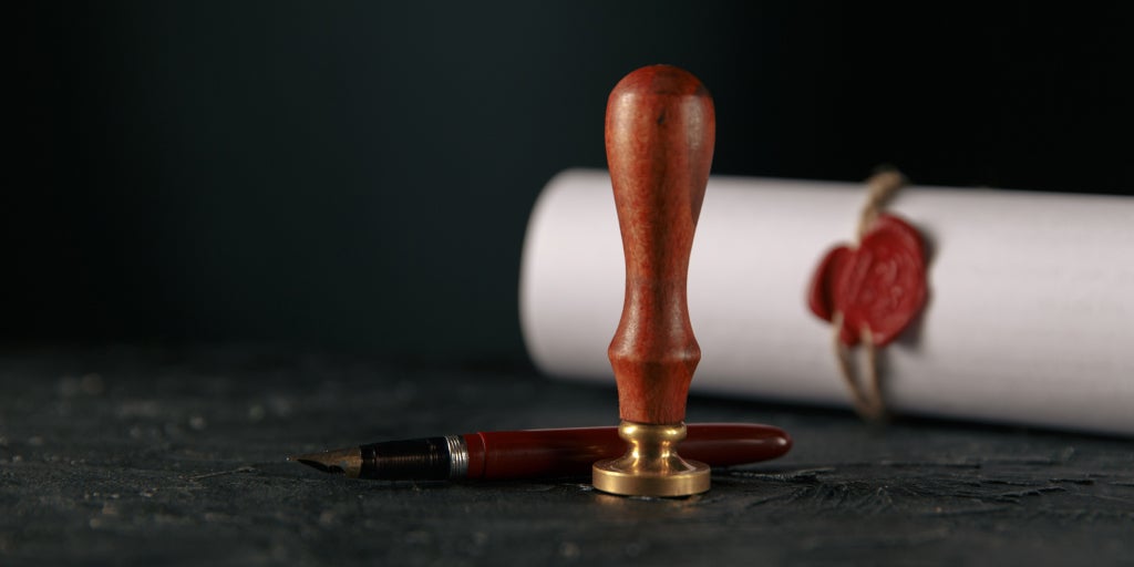Classical stamp sitting in front of an old fountain pen with scroll behind it