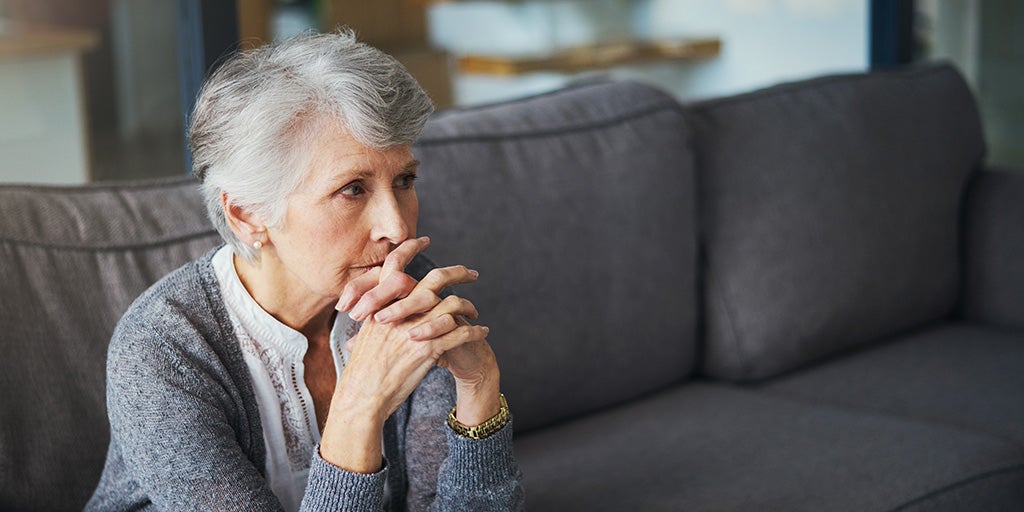 Elderly woman sitting anxiously on her sofa