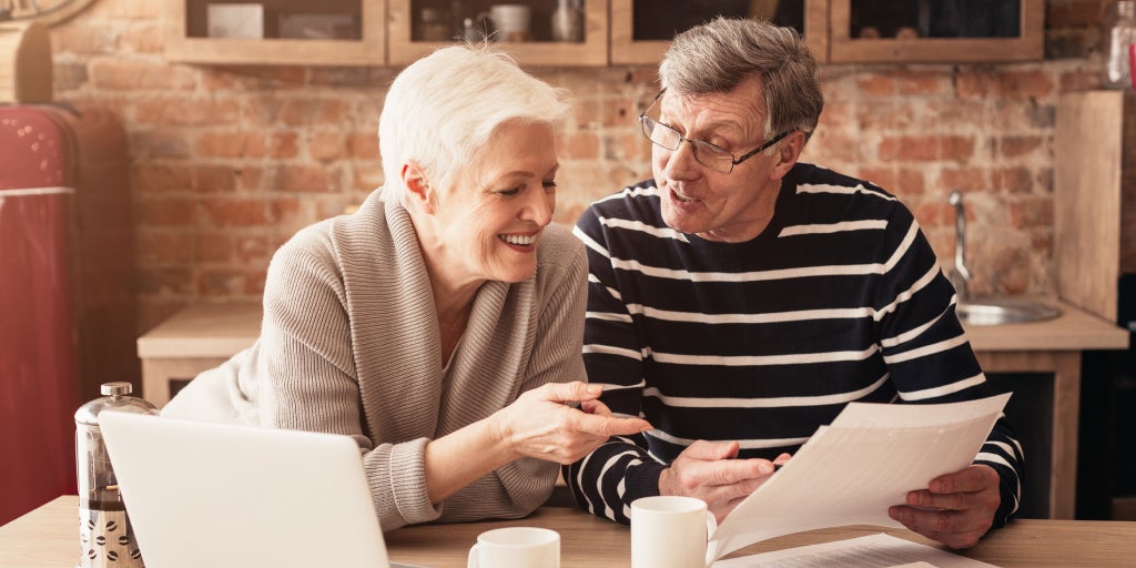Joyful looking senior couple reviewing documents as they sit at the kitchen table