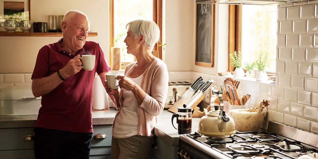 Elderly couple standing in their kitchen and enjoying a cup of coffee