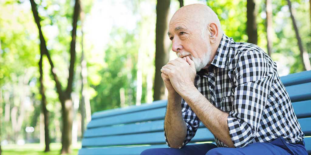 Man sitting on park bench with his hand clenched together over his mouth