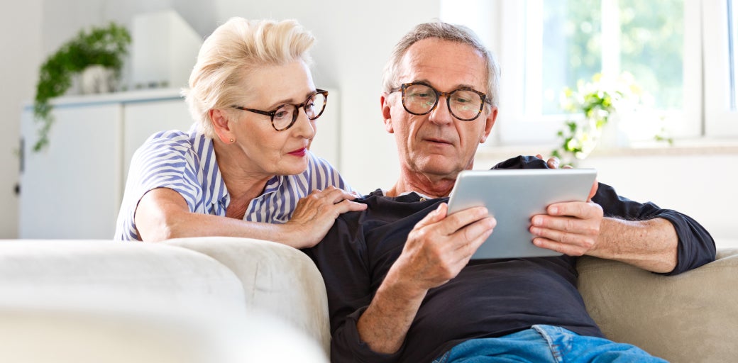 Man and woman sitting on sofa whilst reading information on their tablet device