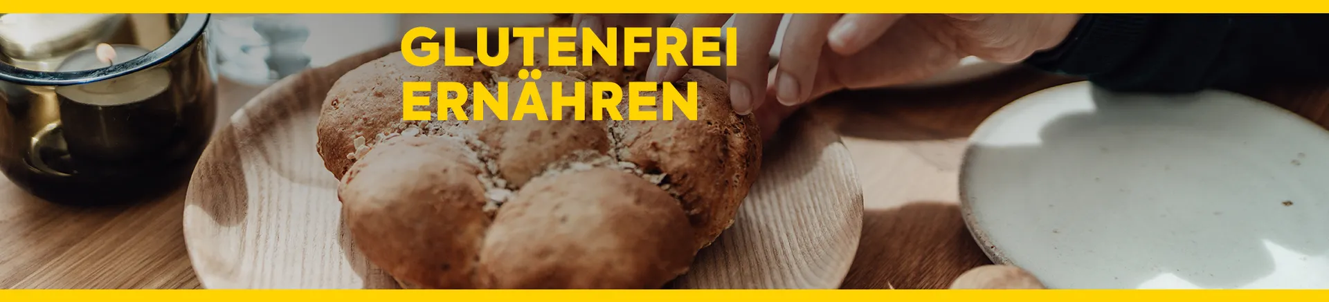 Person reißt ein Stück von einem glutenfreien Weckerl ab, das auf einem Holzteller liegt. Text: Glutenfrei ernähren